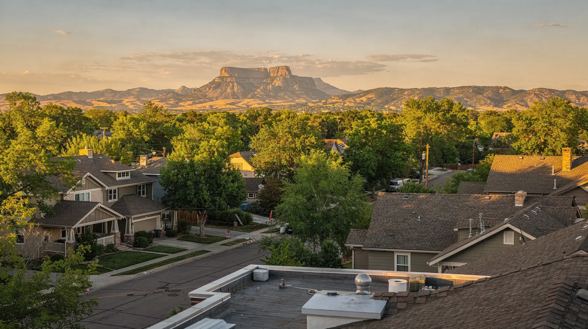 Rooftop view across tree-lined Fort Collins streets toward the foothills at golden hour
